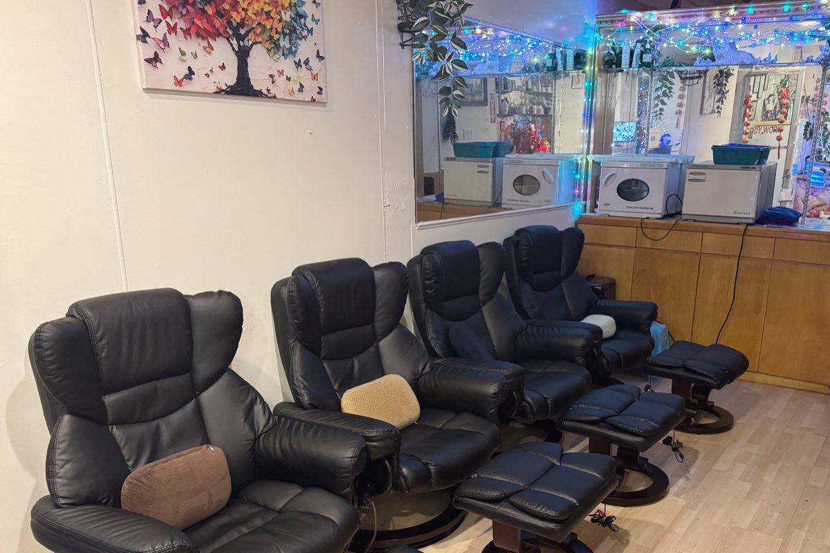 The foot-massage room at Elizabeth Spa: four black reclining chairs with footstools along a wall, a butterfly-tree painting, and a counter of hot-towel warmers under a mirrored wall strung with fairy lights.